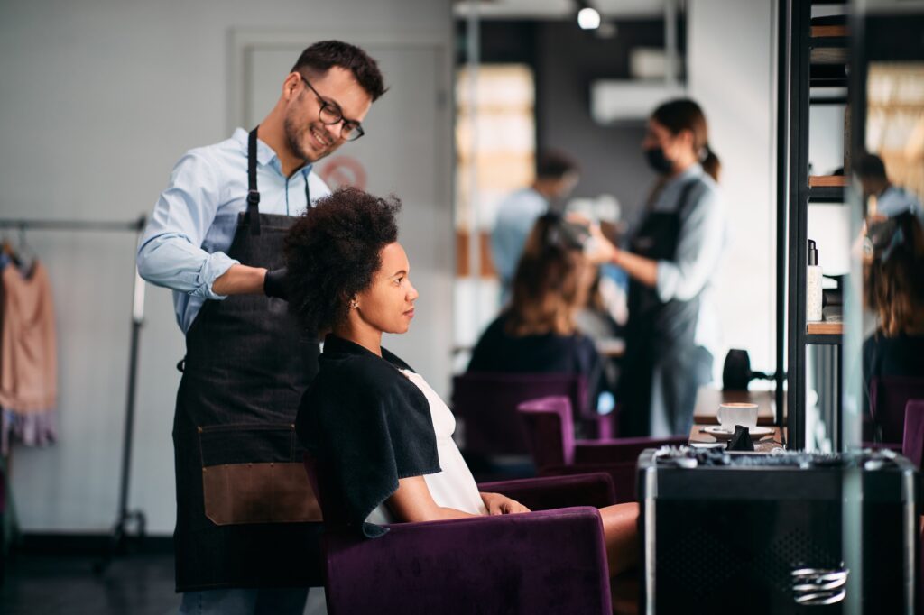 African American woman getting her hair styled by hairdresser at the salon.